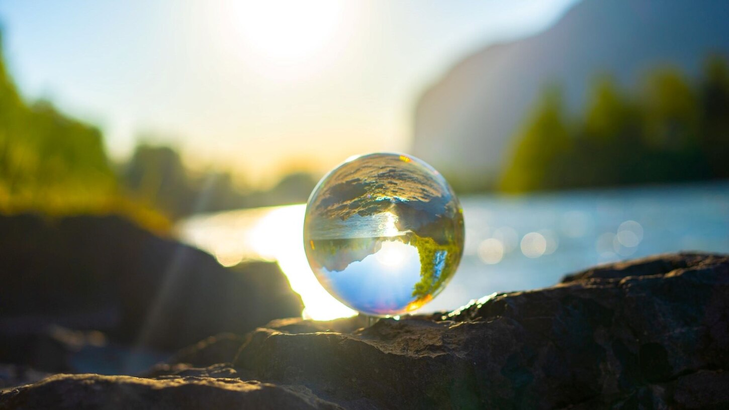 Glaskugel auf einem Stein liegend am See mit Spiegelung der Umgebung bei Sonnenschein